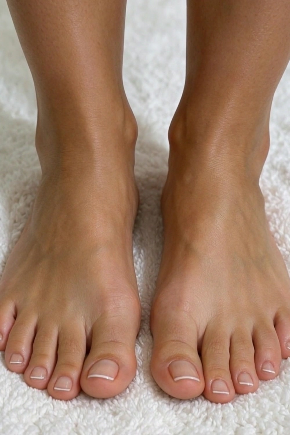 Bare feet with a skinny french tip pedicure on a soft white mat